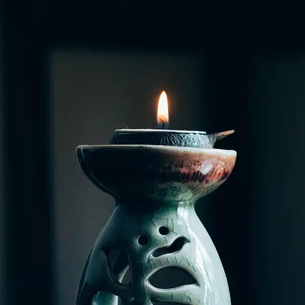 A pierced celadon stoneware lantern with a lit tea light in its dish