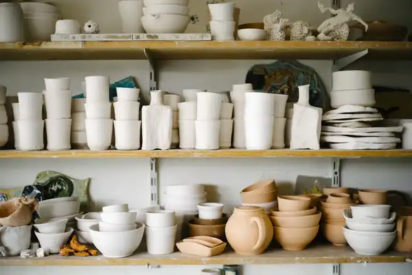 Shelves of white-glazed and unglazed bowls, cups and jugs in a pottery studio