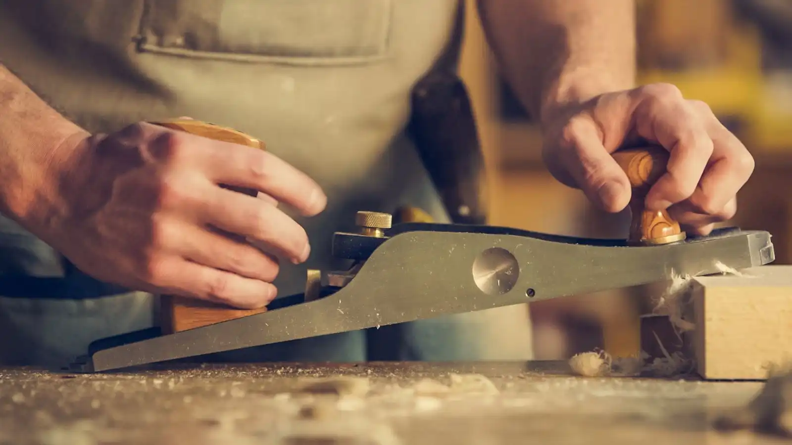 Two hands pushing a hand plane along a board on the bench