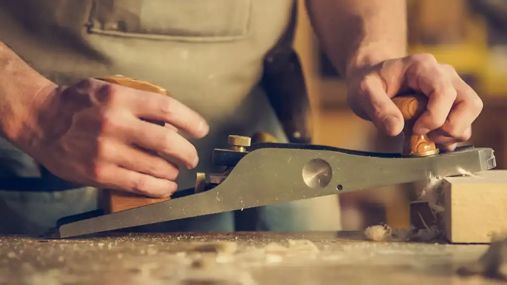 Two hands pushing a hand plane along a board on the bench