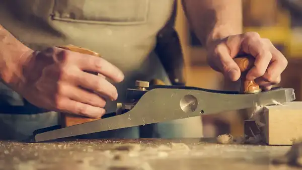 Two hands pushing a hand plane along a board on the bench