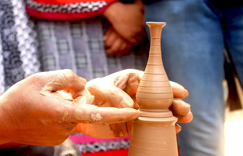 Two hands shaping a tall clay bottle on a turning wheel