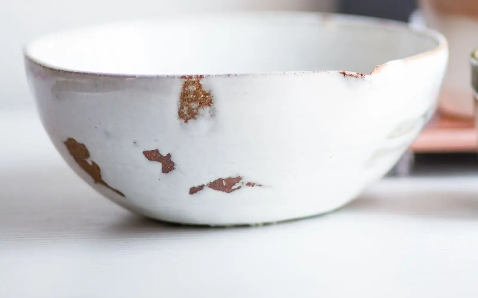 A white glazed bowl with worn patches on its rim beside a small cup
