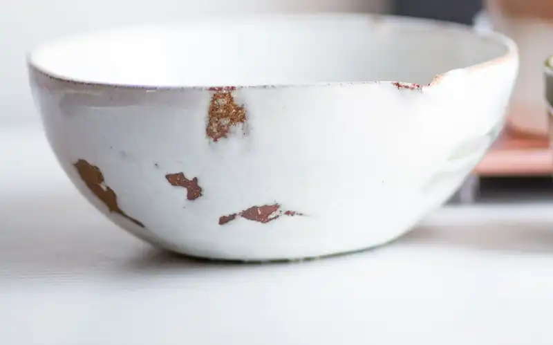 A white glazed bowl with worn patches on its rim beside a small cup