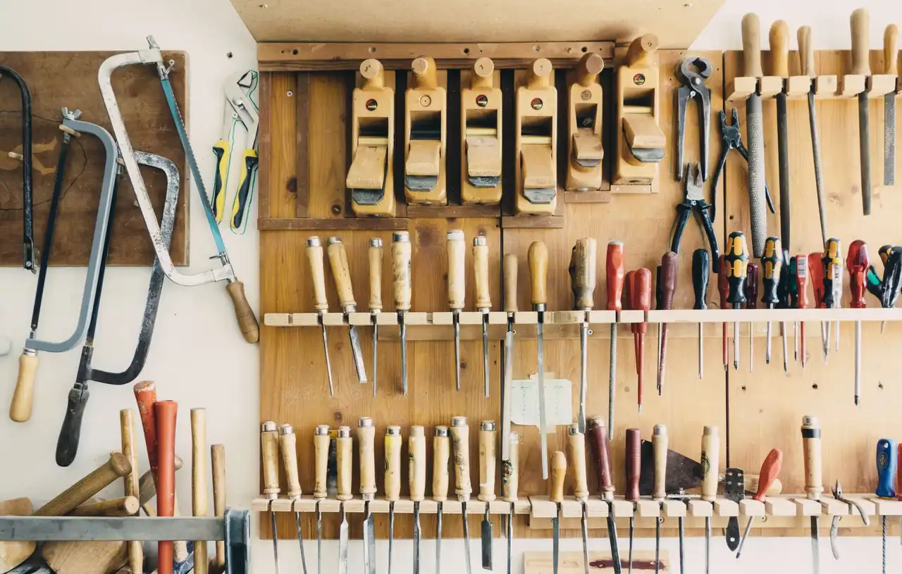 A pegboard wall of chisels, saws, hand planes and pliers above a workbench